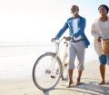 an image of a smiling couple walking two bicycles along the beach