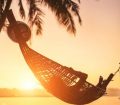 Hammock between palm trees on sandy beach at sunset