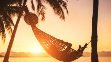 Hammock between palm trees on sandy beach at sunset