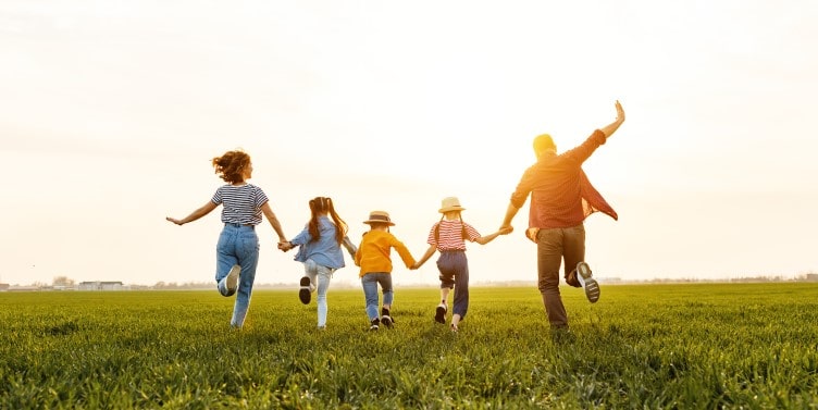 Family holding hands running on a field in summer